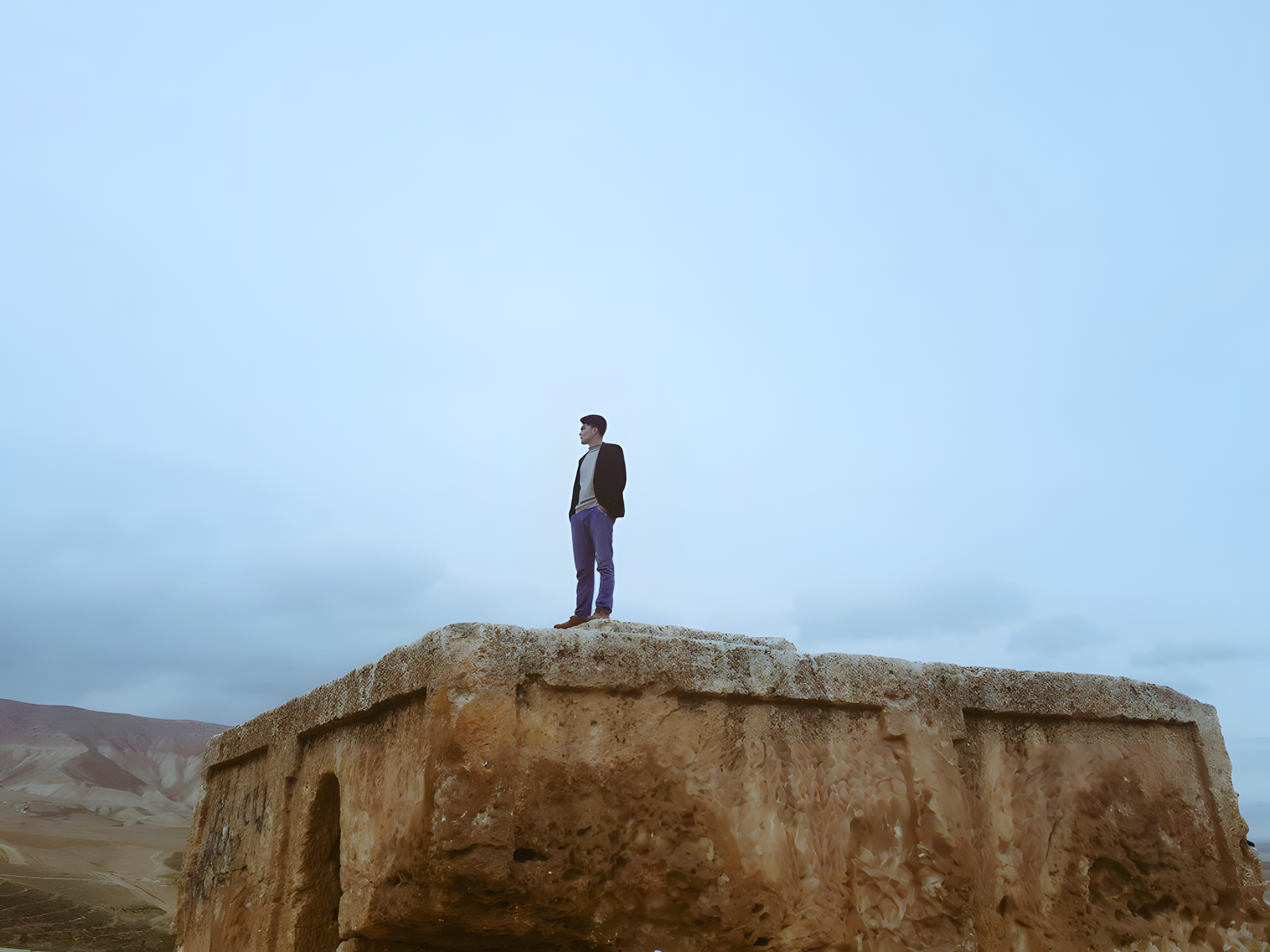 Zamanuddin Zafar standing on an ancient stone monument, mountains beyond